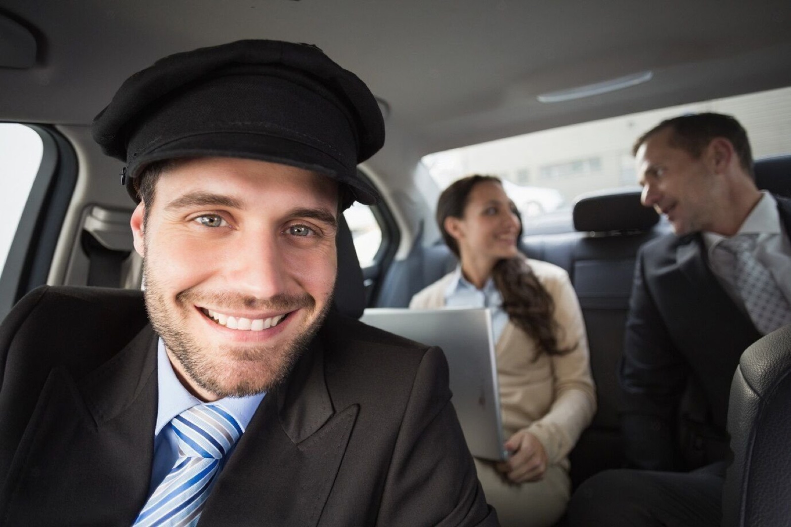 Smiling chauffeur driving an executive car with passengers working in the back seat