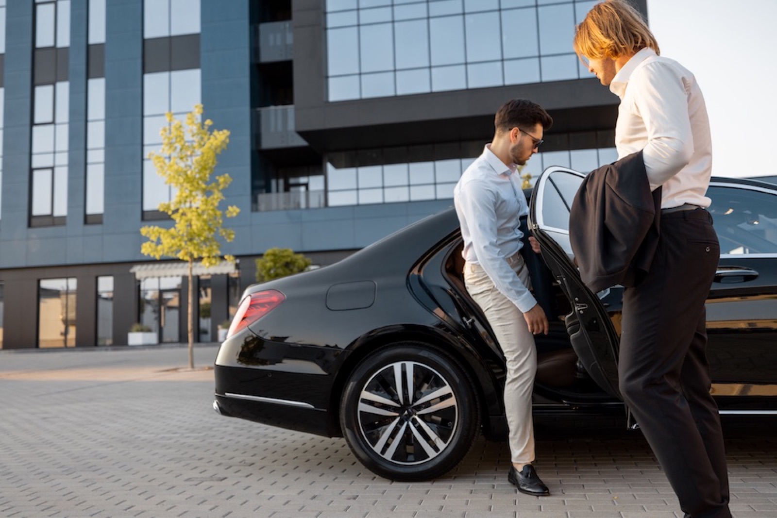 Chauffeur assisting a passenger out of an executive car near a London attraction
